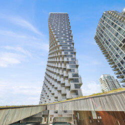 Two modern high-rise buildings with staggered balconies rise against a clear blue sky, featuring glass façades and white panels.