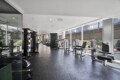 Well-lit gym with cardio and strength machines along large glass walls and a city view outside.