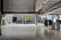 Industrial lobby reception with concrete ceiling, exposed pipes, and a vertical garden behind a dark desk where three people stand talking.
