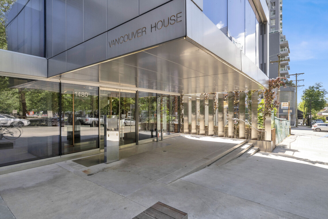 Front view of a modern glass-and-metal building with 'Vancouver House' on the facade and a glass entryway toward the street.
