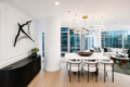 Open-concept living and dining space in a modern high-rise, featuring a white marble dining table, white chairs, and circular gold pendant lights.