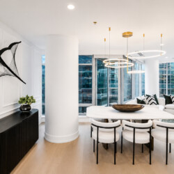 Open-concept living and dining space in a modern high-rise, featuring a white marble dining table, white chairs, and circular gold pendant lights.