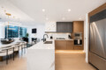 Open-concept kitchen and living area in a modern high-rise apartment with a marble island, wooden cabinets, and stainless steel appliances.