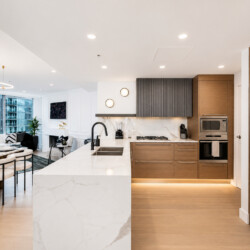 Open-concept kitchen and living area in a modern high-rise apartment with a marble island, wooden cabinets, and stainless steel appliances.