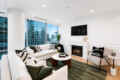 Modern living room with a white sectional, green cushions, a round marble coffee table, and a fireplace, seen from a cozy seating area with a city view.