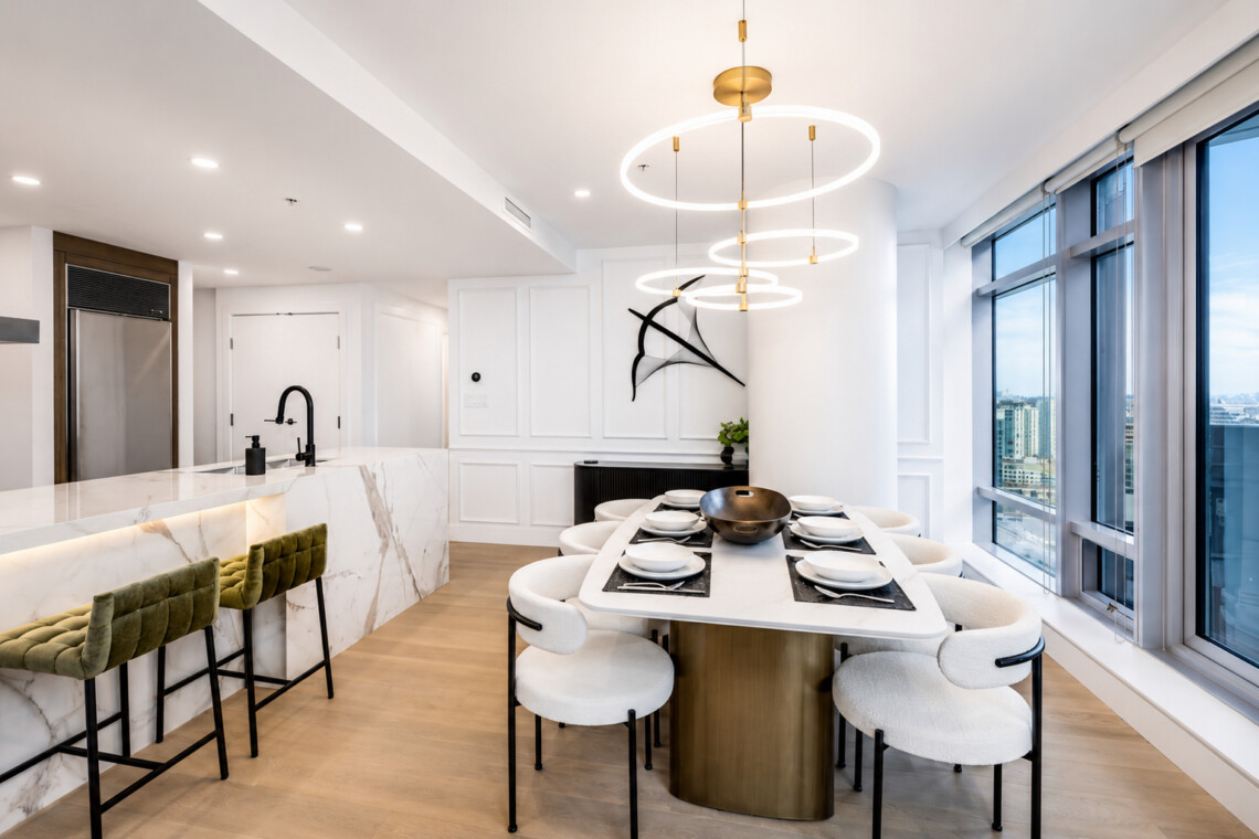 Open-concept kitchen and dining area with marble island, circular pendant lights, and large windows overlooking the city.
