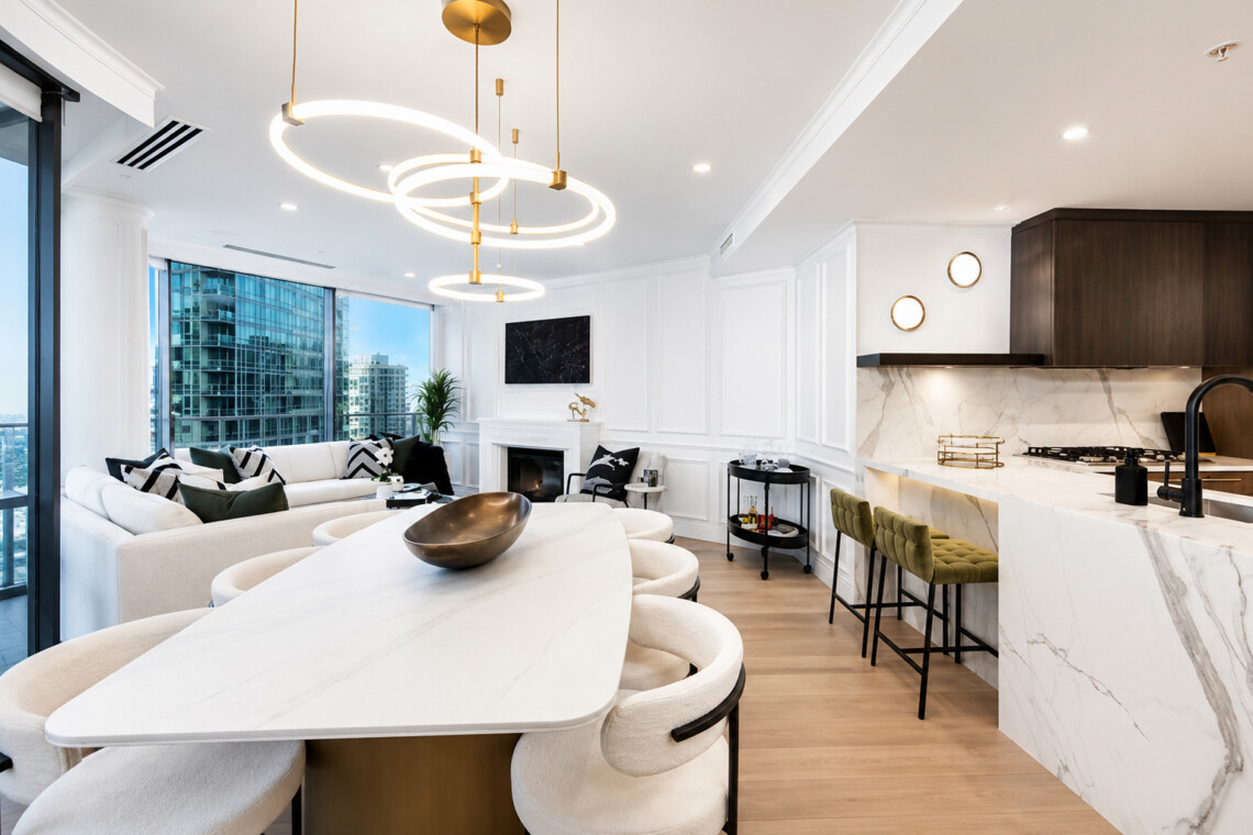 Open-concept living area with marble kitchen counter, circular gold pendant lights, and a beige sofa facing large city windows.