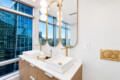 Luxurious modern bathroom with double vessel sinks, marble countertop, gold faucets, and tall mirrors overlooking a city skyline.
