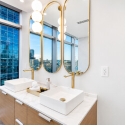 Luxurious modern bathroom with double vessel sinks, marble countertop, gold faucets, and tall mirrors overlooking a city skyline.