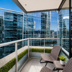 Balcony with brown wicker chairs and a small table plant, overlooking reflective glass skyscrapers.