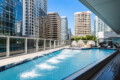 Rooftop pool with loungers and cabanas, surrounded by glass-walled skyscrapers against a blue sky