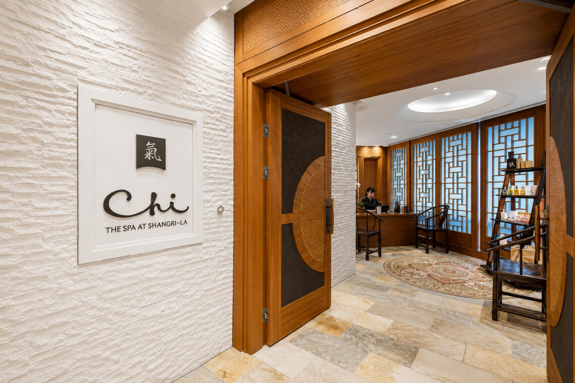 Wooden doorway opens to a spa reception with a desk, chairs, and a curved rug.
