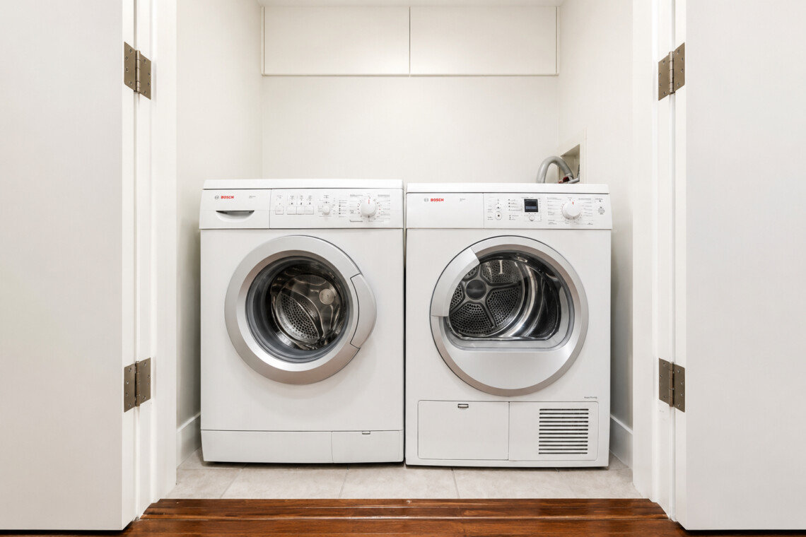 White front-loading washing machine and dryer side by side in a compact laundry closet with white upper cabinets above them