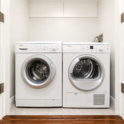 White front-loading washing machine and dryer side by side in a compact laundry closet with white upper cabinets above them