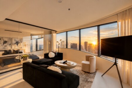 Sunset-lit modern living room with black sofas, a round coffee table, and a wall of curved windows overlooking the city skyline.