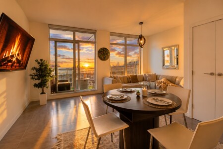 Living/dining room bathed in warm sunset light with a round dining table set for four and a gas fireplace on the left.