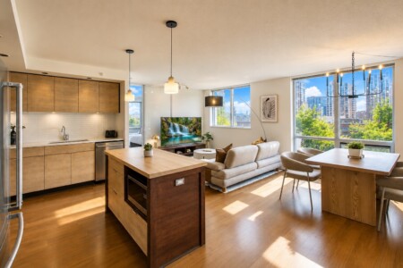 Open-concept living area with kitchen, island, dining table, and a sofa facing a TV, daylight from large windows