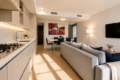 Open-concept living area with a light wood kitchen on the left, a gray sofa and a wall-mounted TV on the right, and a dining table in the back.