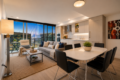 Open-concept living area with a white dining table and black chairs, a gray sofa, and a balcony overlook of a city skyline at dusk