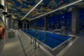 Indoor pool area in a modern gym at night, with a colorful patterned ceiling, bright linear lights, and city lights visible through large windows.