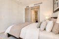Hotel bedroom with a large bed, beige bedding and pillows; open doorway reveals an en suite bathroom in the background.
