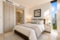 Bright contemporary bedroom with a king bed, two nightstands, lamps, and a city skyscraper view through a large window.