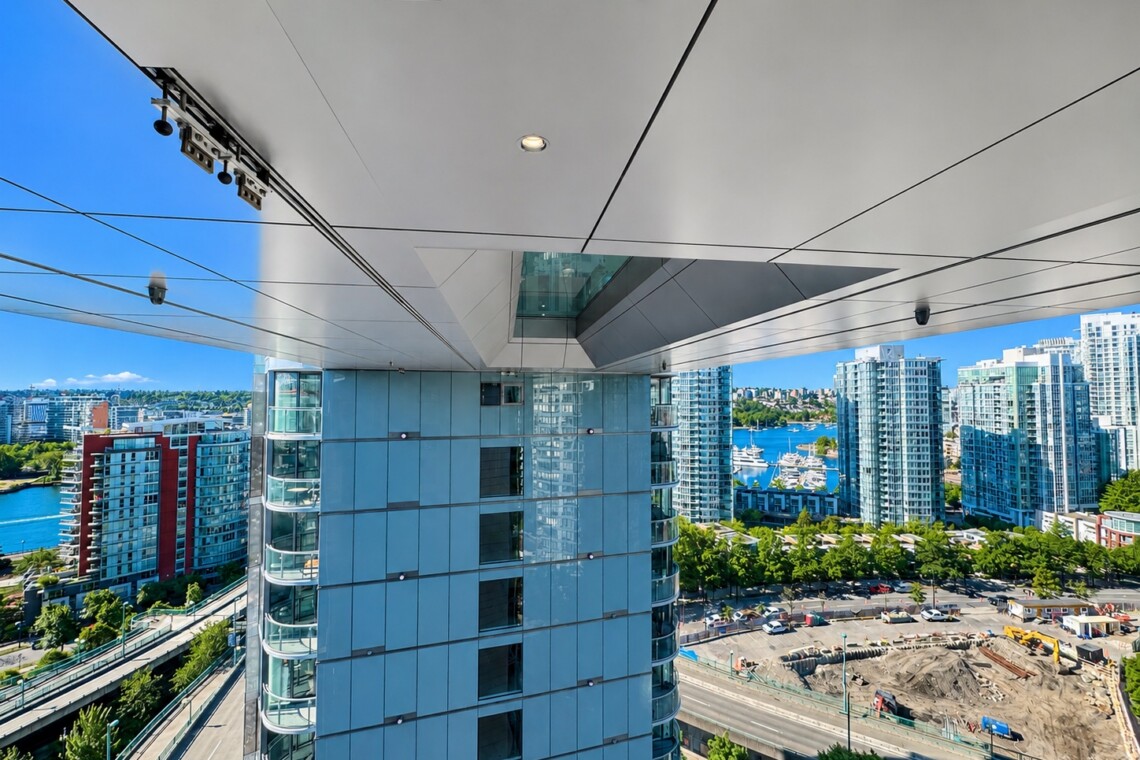 High-angle view of a modern city skyline with glass towers, a marina with boats, and a construction site below, seen from beneath a large overhang.