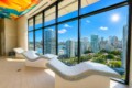 Indoor wellness lounge with curved mosaic-tile loungers facing large windows overlooking a sunny city skyline and marina.