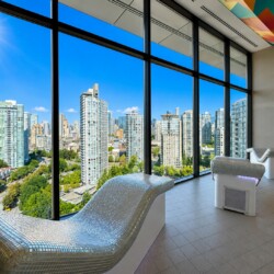 Indoor spa lounge with two curved mosaic-tile chaise lounges facing floor-to-ceiling windows overlooking a sunny city skyline.
