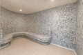 Curved mosaic-tiled steam room with built-in bench along the walls, illuminated by recessed ceiling lights.