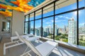 Indoor lounge area with white sunbeds and a bright multi-colored geometric ceiling, overlooking a city skyline through floor-to-ceiling windows