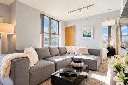 Bright modern living room with a gray sectional sofa, white pillows, and a glass coffee table