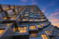 Low-angle view of a high-rise with stacked glass balconies glowing at sunset.