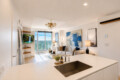 Open-concept living area with a white kitchen island, stainless sink, sofa, abstract blue art, and a balcony view of the city.