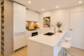 Bright modern kitchen with white cabinets, an island sink, and two white bar stools.