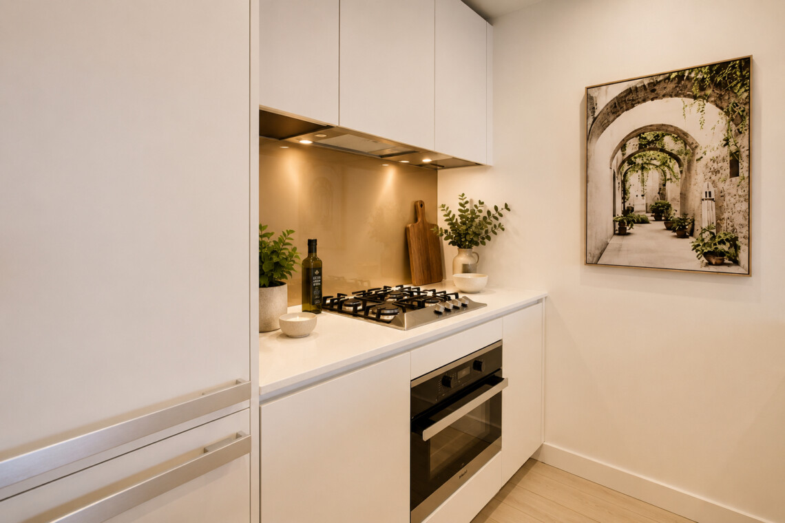 Modern white kitchen with a stainless gas cooktop, built-in oven, and under-cabinet lighting surrounded by green plants on the counter.