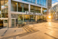 Modern glass-front Fresh Market storefront in a sunny urban plaza with stairs and metal railings outside
