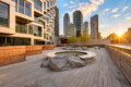 Rooftop courtyard with circular planter water feature, wooden deck, and modern high-rise buildings at sunset.