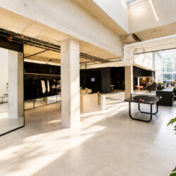 Open-plan retail space with concrete pillars, clothing racks along the left, a ping-pong table in the foreground, and large windows flooding the area with light.