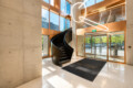 Modern building lobby with a black spiral staircase, copper trim, large windows, and a looping neon sculpture above the entrance.