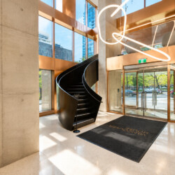 Modern building lobby with a black spiral staircase, copper trim, large windows, and a looping neon sculpture above the entrance.