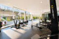 Bright modern gym with rowers and stationary bikes by large windows overlooking an urban exterior likely a transportation area outside the glass walls.