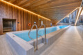Indoor pool in a modern wooden atrium with warm ceiling lights and stainless handrails beside a calm blue pool