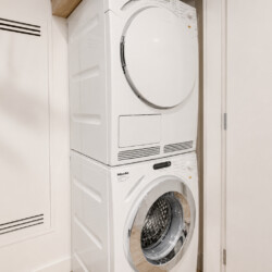 Stacked front-loading washing machine below a clothes dryer in a narrow laundry closet.