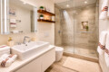 Modern bathroom with a white double sink, large backlit mirror, and glass-enclosed shower. It features wood shelves, plants, and beige tiling.
