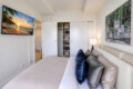 Modern bedroom with a wall-mounted flat-screen TV, open closet shelves, and a beige bed with multiple pillows.