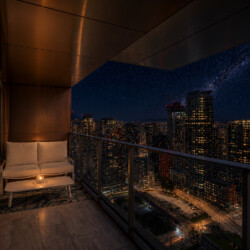Night city view from a balcony with a beige outdoor sofa and candlelight, overlooking a lit downtown skyline at night.