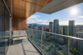 Balcony lounge with white cushioned seating and a glass railing overlooking a dense city skyline under a sunny sky.