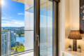 Hotel room with a sliding glass door open to a balcony, offering a river and city skyline view on a sunny day.