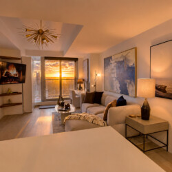Sunset view through large windows into a modern living room with a white sofa and abstract art.